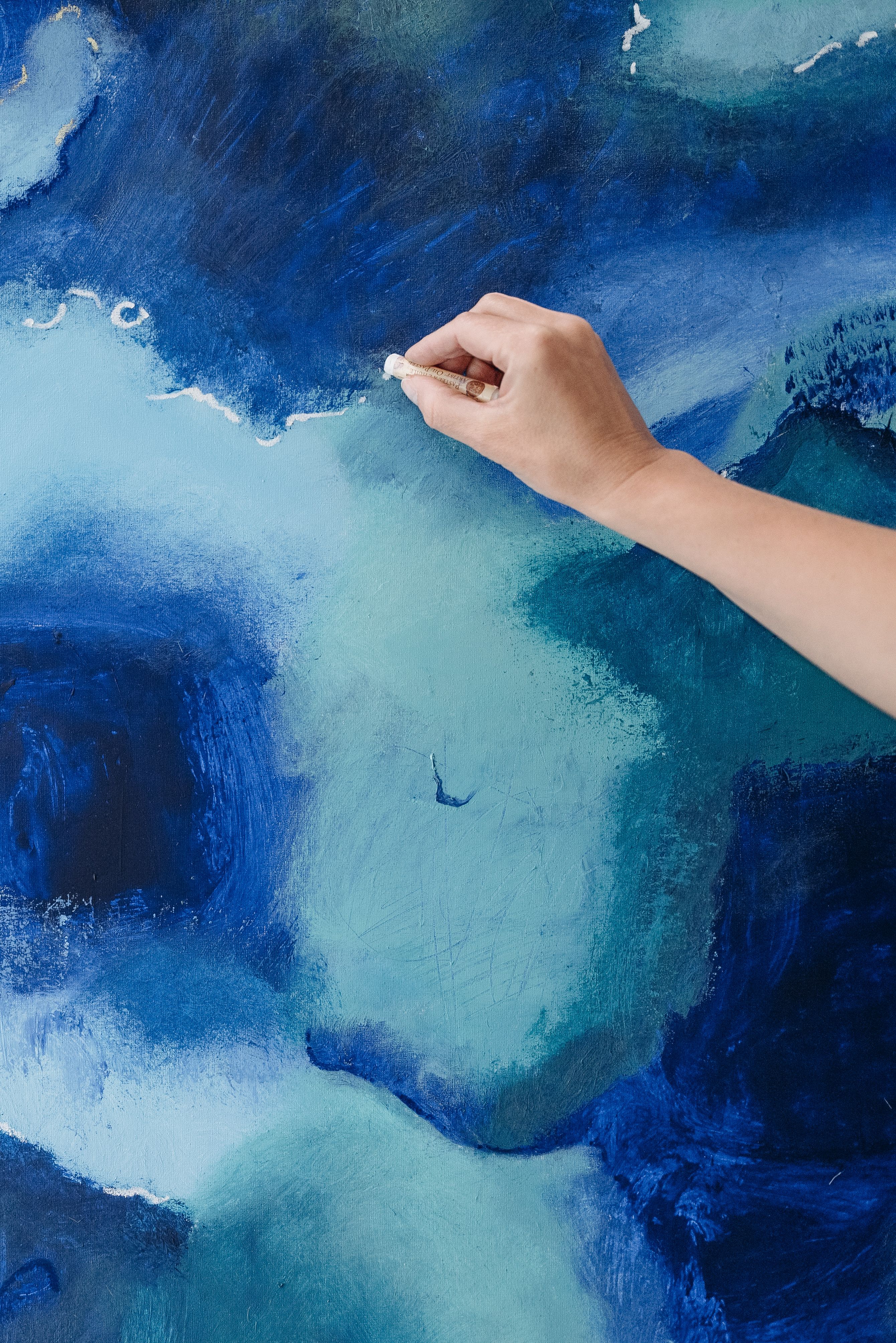An artist’s hand making marks on a richly textured blue abstract painting